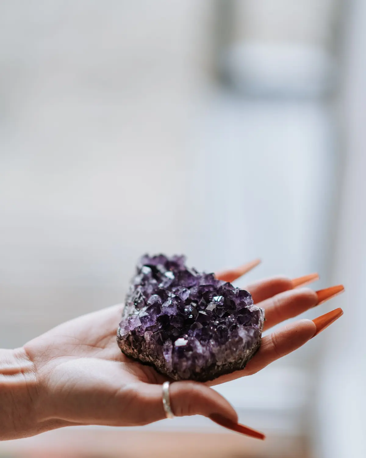 A hand holding a rough amethyst in a sunlit room