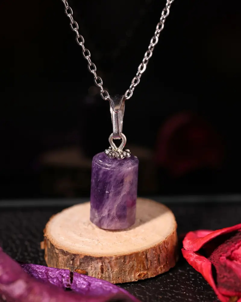 An amethyst pendant on a silver chain, displayed on a wood slice