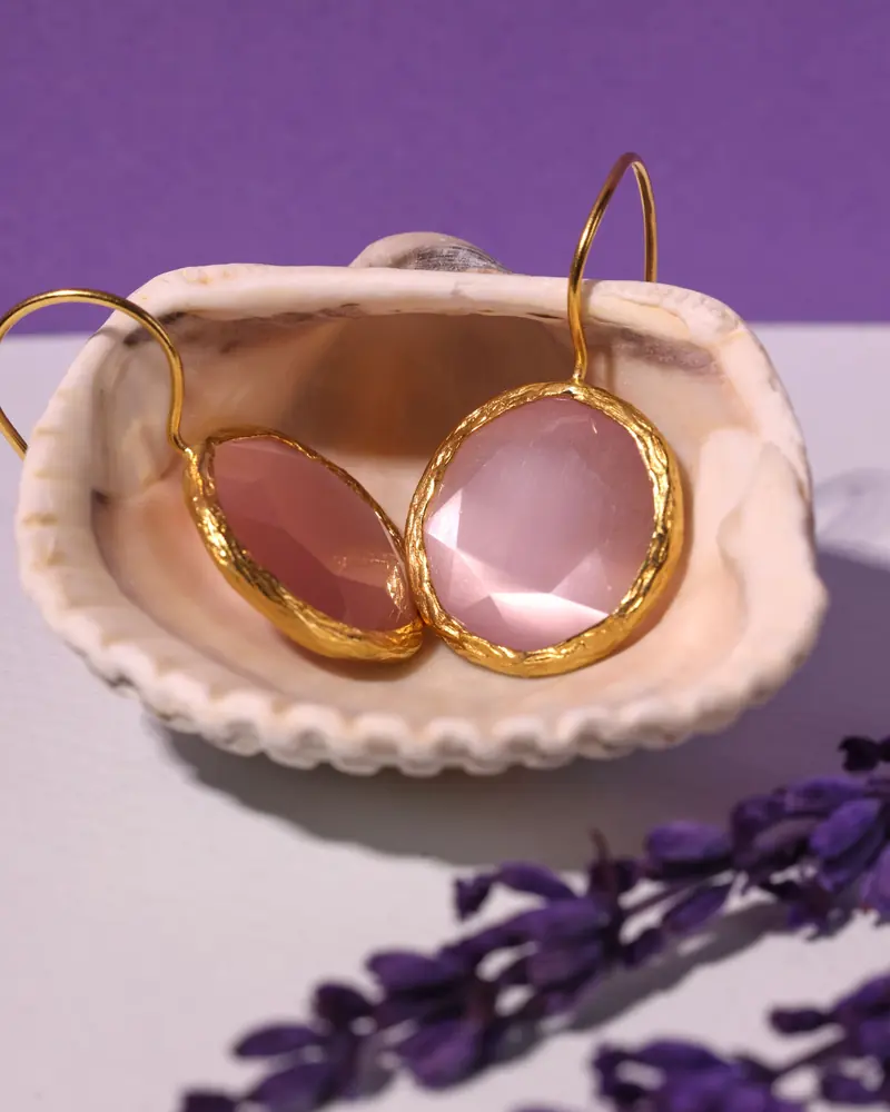 Pink gemstone earrings in gold-tone bezels, resting in a seashell