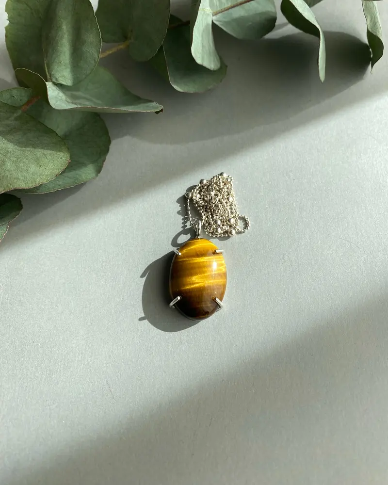 A tiger's eye oval pendant on a chain with eucalyptus leaves