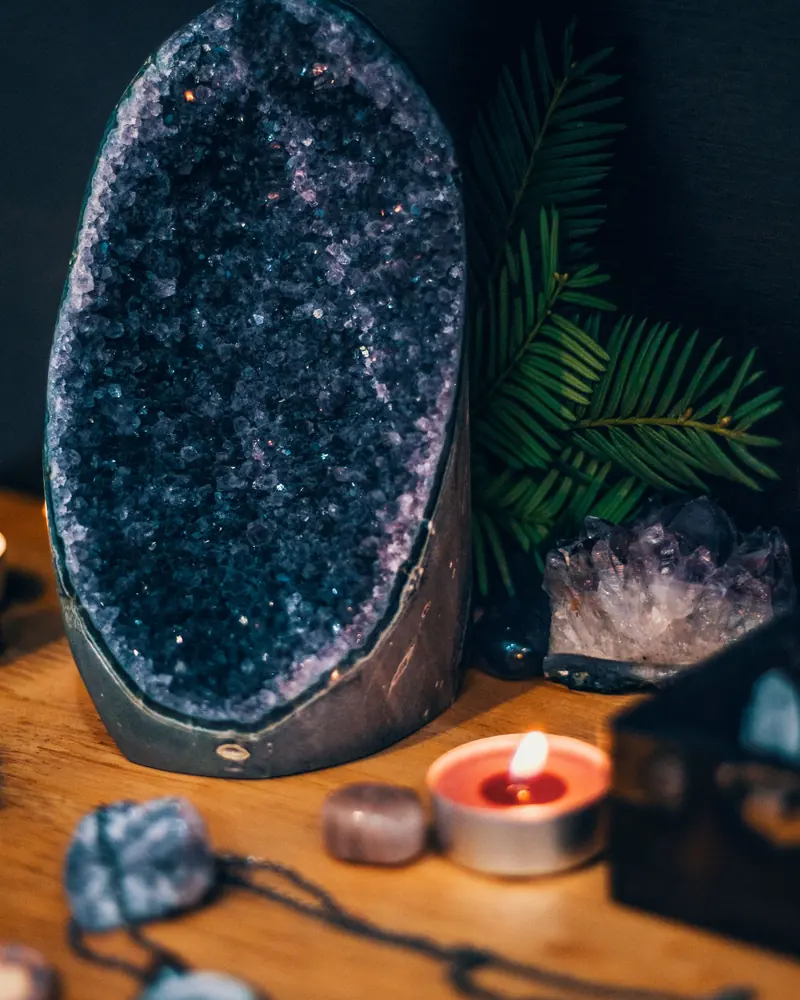A tall dark amethyst cathedral geode beside candles