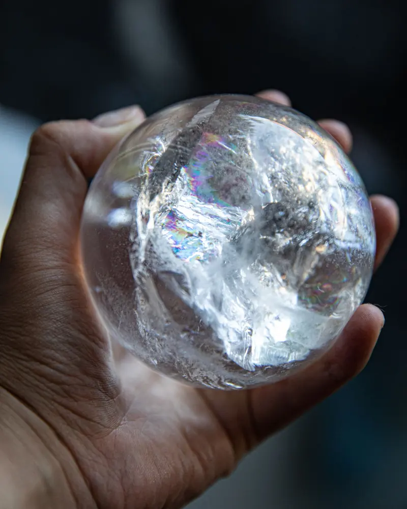 A clear quartz sphere held in a hand, catching rainbows