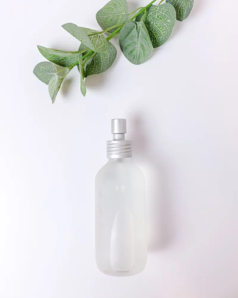 A frosted glass spray bottle with eucalyptus