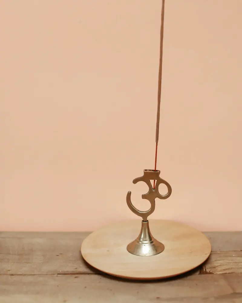An incense stick in a brass Om holder on a wooden base