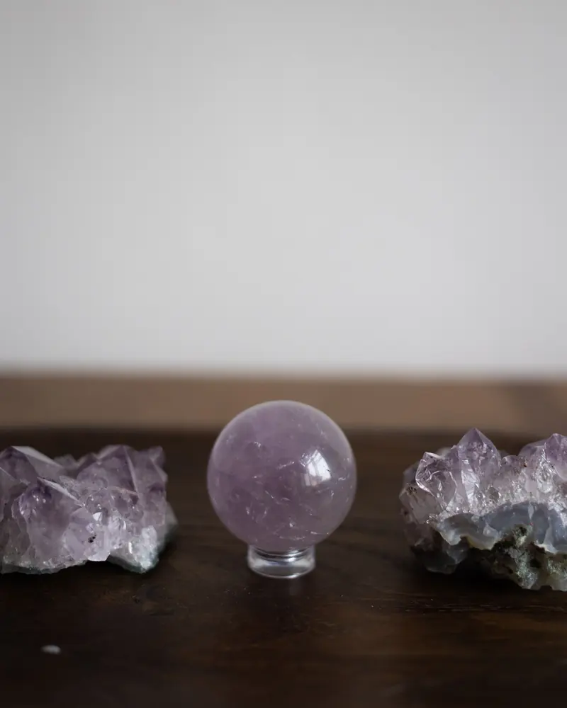 A polished amethyst sphere between two amethyst clusters