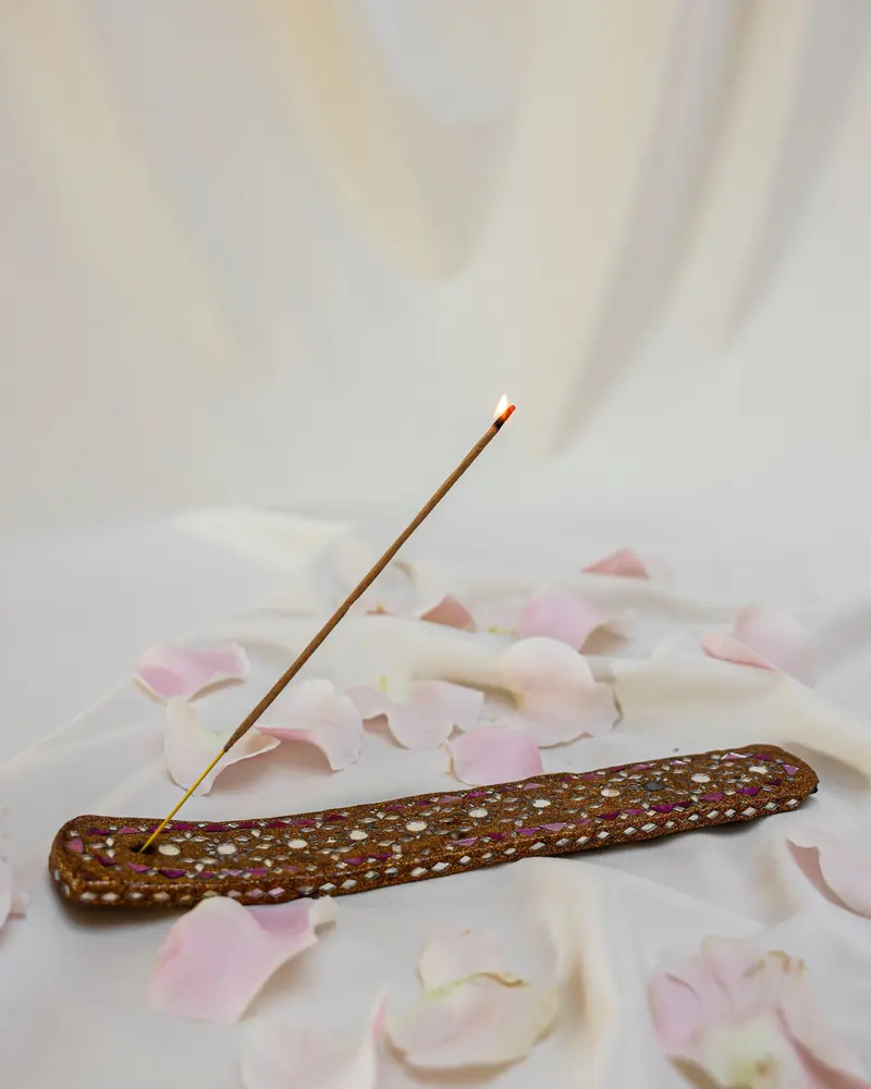 A burning incense stick in a wooden holder among rose petals