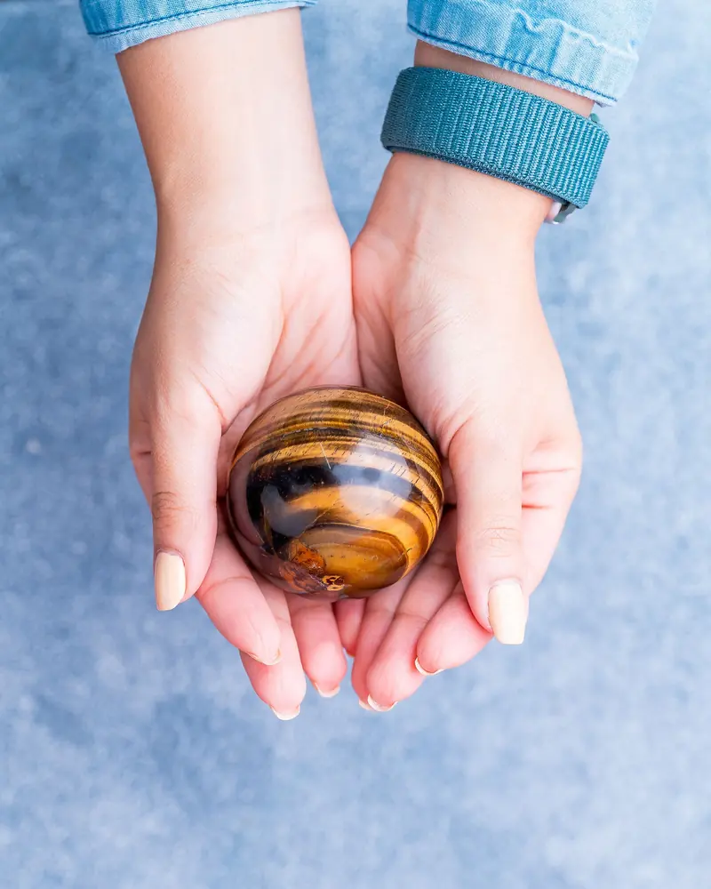 A polished tiger's eye sphere held in two hands