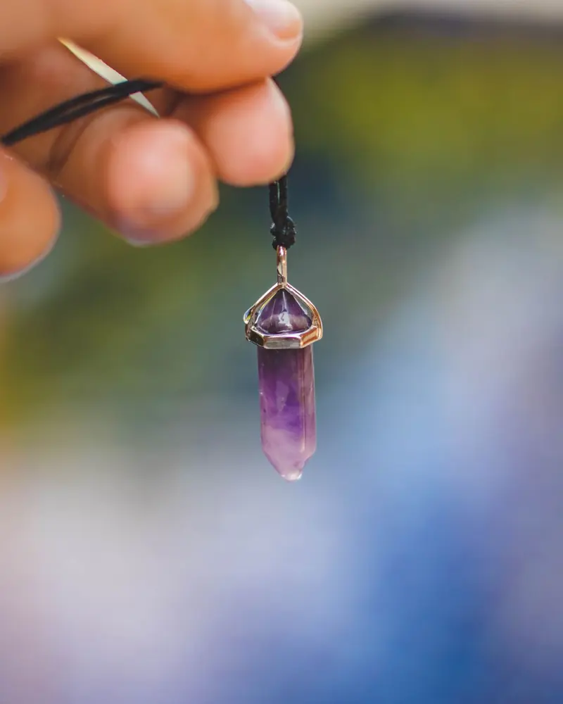 An amethyst point pendant held up on a black cord